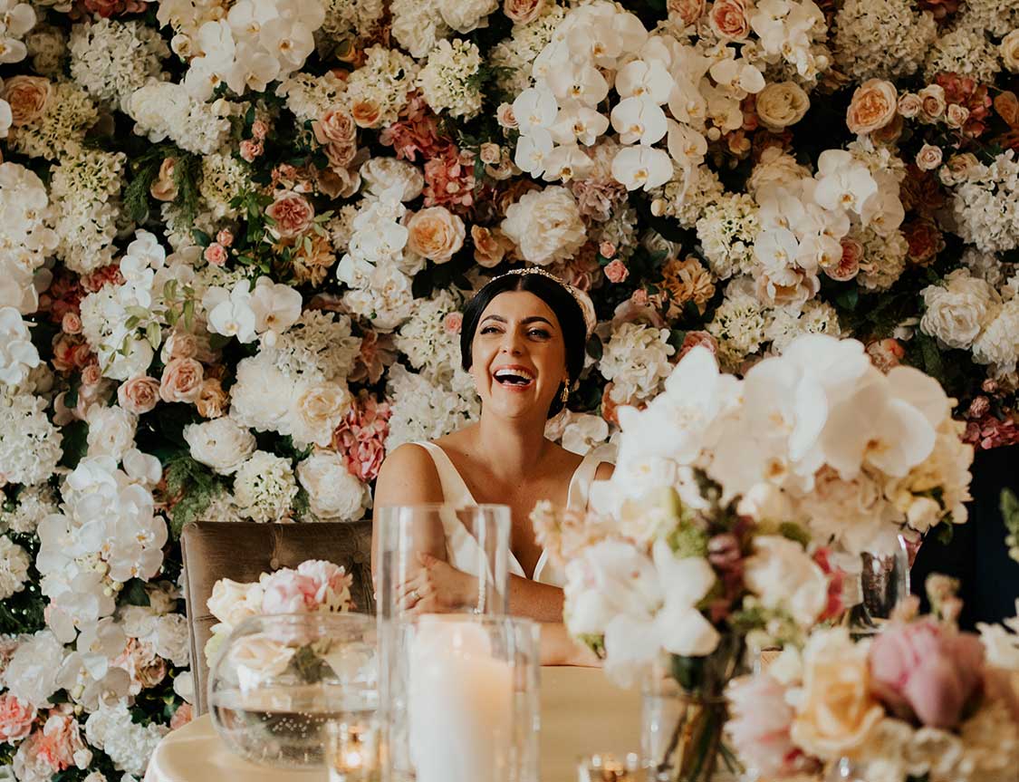 Laughing bride in front of flower wall